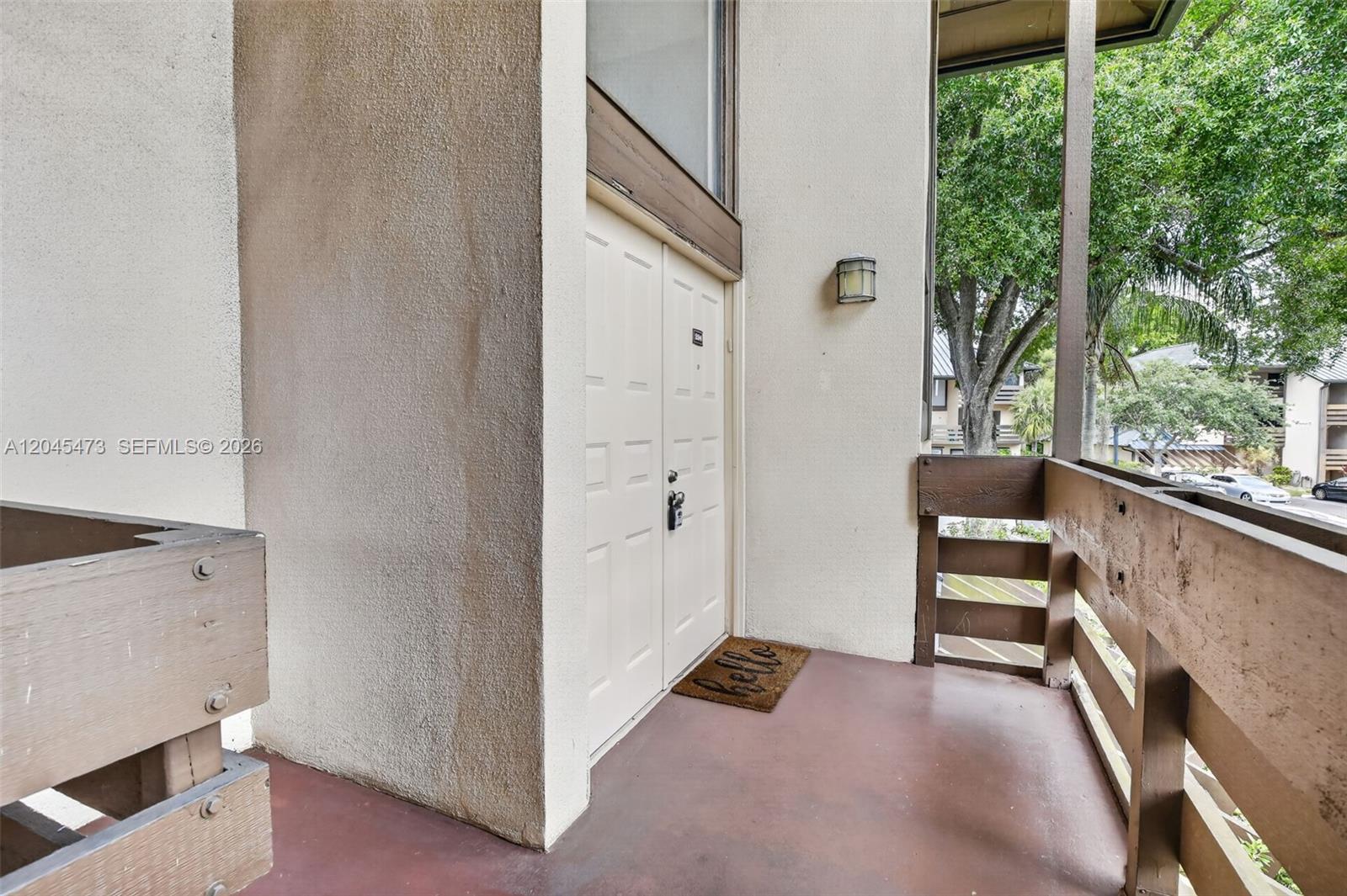 A covered balcony features a double door entrance, a brown doormat, and wooden railings — 120 SW 96th Ter # 204, Plantation FL 33324, PLANTATION, FL