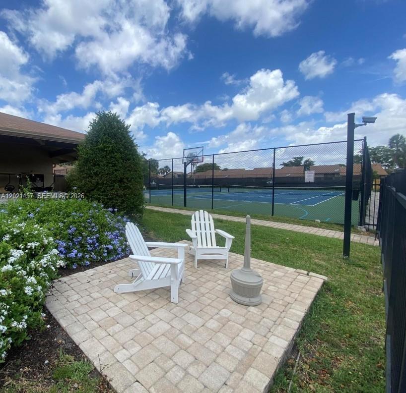 Two white Adirondack chairs sit on a brick patio beside a fenced tennis court — 8015 SW 21st Ct, Davie FL 33324, DAVIE, FL