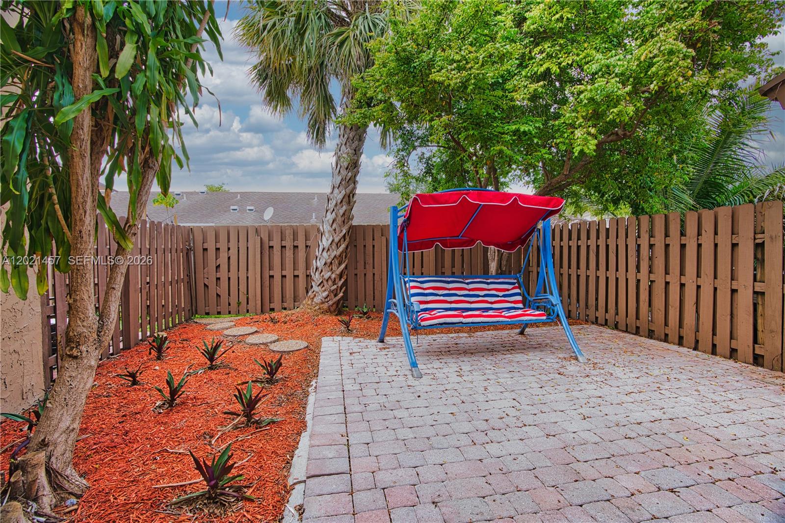 A backyard patio features a red and blue swing, mulch landscaping, and a wooden fence — 8015 SW 21st Ct, Davie FL 33324, DAVIE, FL