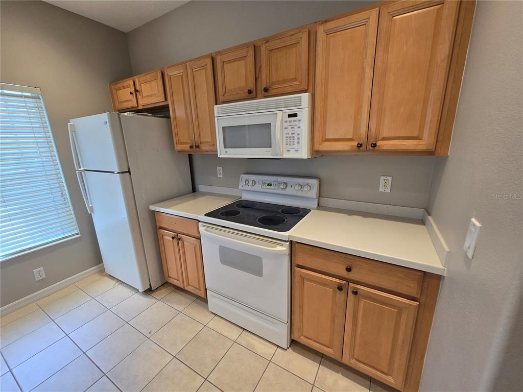 A kitchen features light wood cabinets, white appliances, a white countertop, and tiled flooring — 13088 TIGERS EYE DRIVE, VENICE, FL