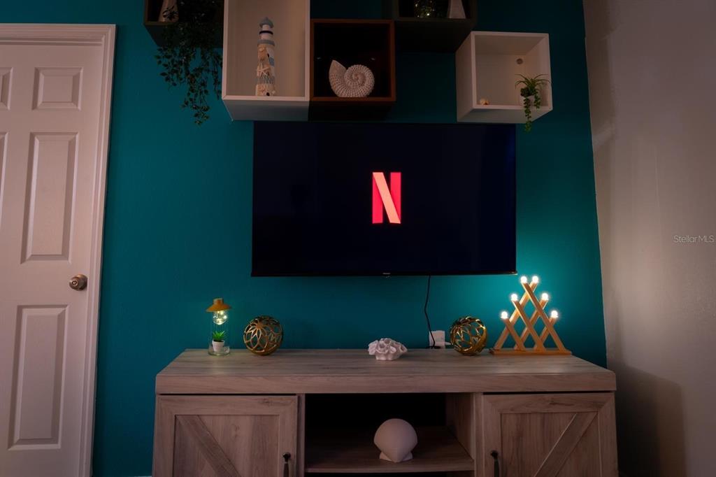 A television mounted on a teal wall above a wooden media console with decorative shelving — 4327 17TH AVENUE S, ST PETERSBURG, FL