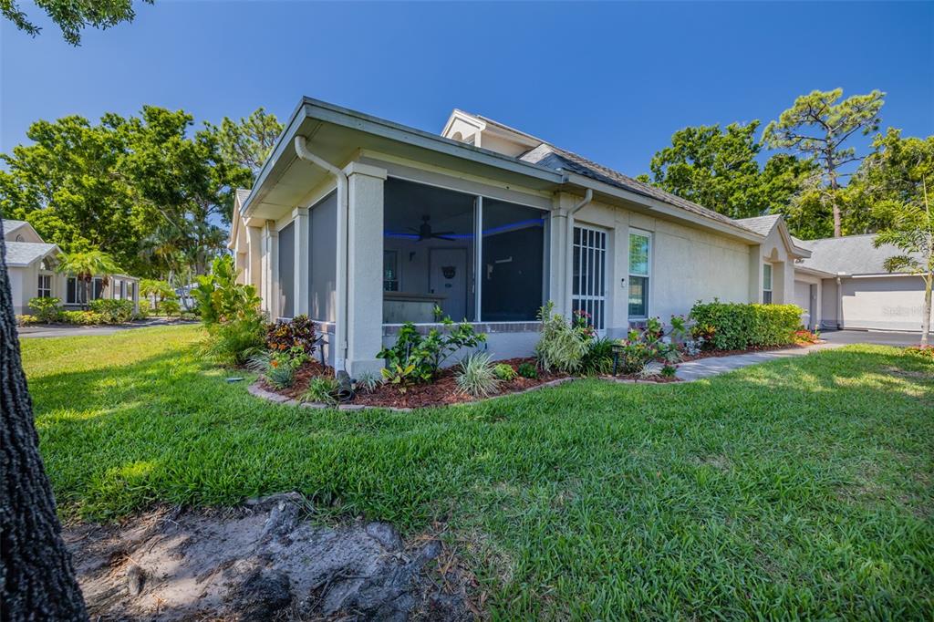 Exterior view of a single-story home with a screened-in porch and landscaped garden beds — 911 GOLFVIEW WOODS DRIVE, SUN CITY CENTER, FL