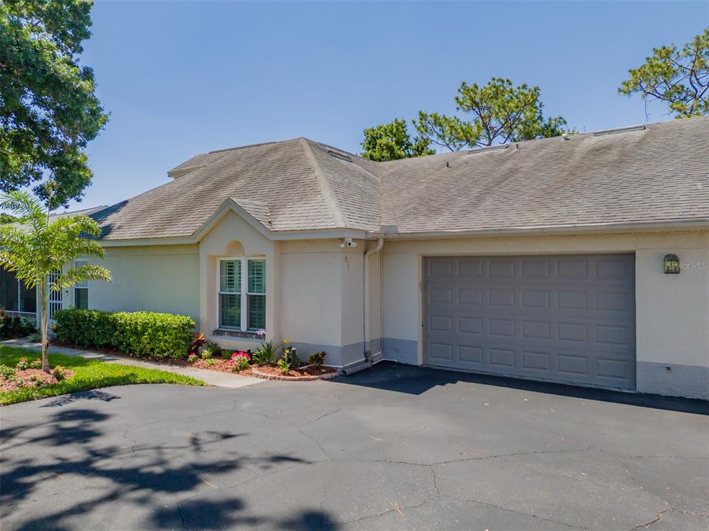 A single-story house with a gray garage door, beige stucco walls, and a shingled roof — 911 GOLFVIEW WOODS DRIVE, SUN CITY CENTER, FL