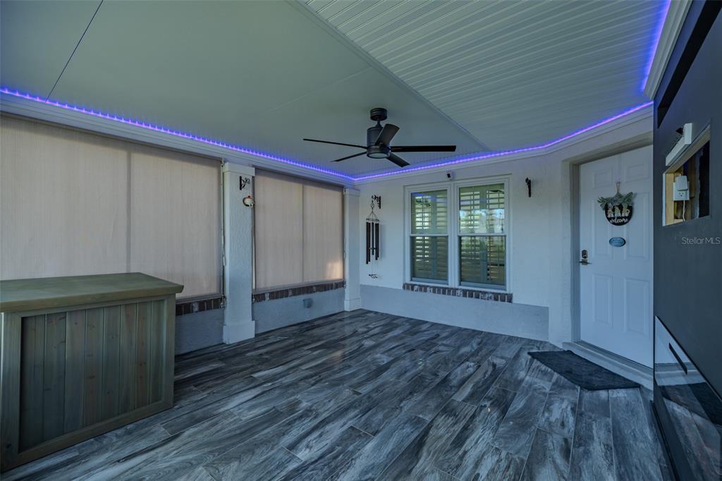 A covered patio features wood-look tile flooring, a ceiling fan, and purple LED accent lighting — 911 GOLFVIEW WOODS DRIVE, SUN CITY CENTER, FL