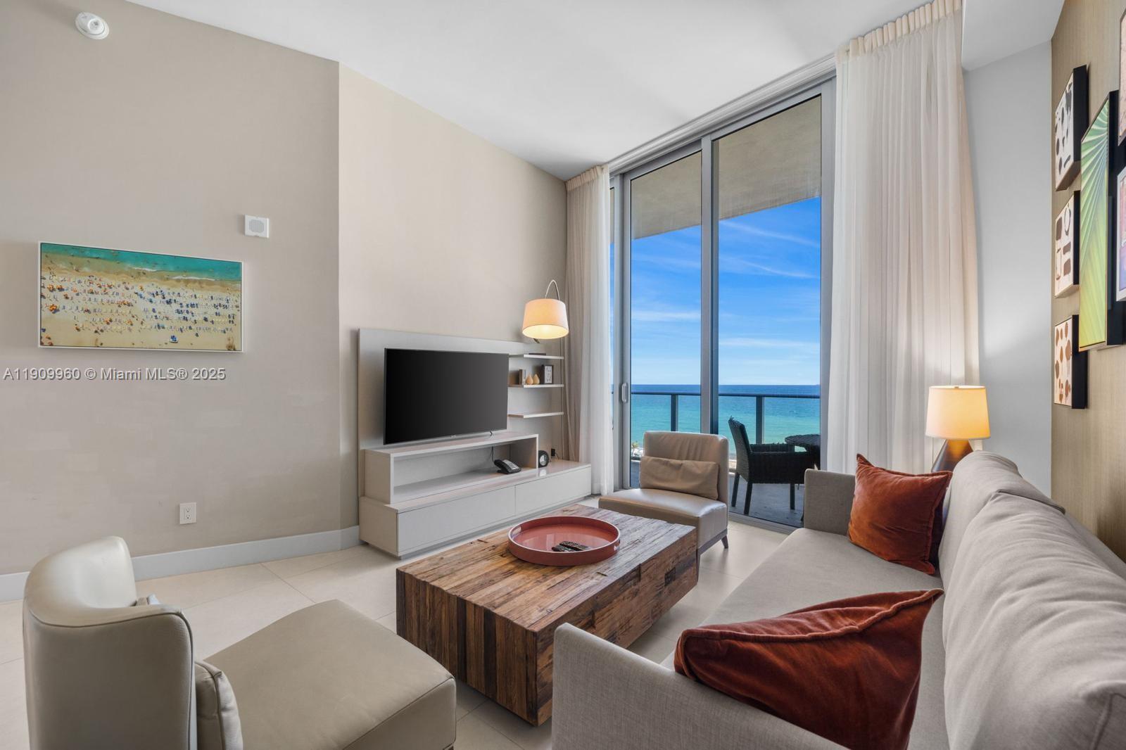 A modern living room features a wooden coffee table, a television, and a balcony view — 4111 S Ocean Dr # 502, Hollywood FL 33019, HOLLYWOOD, FL