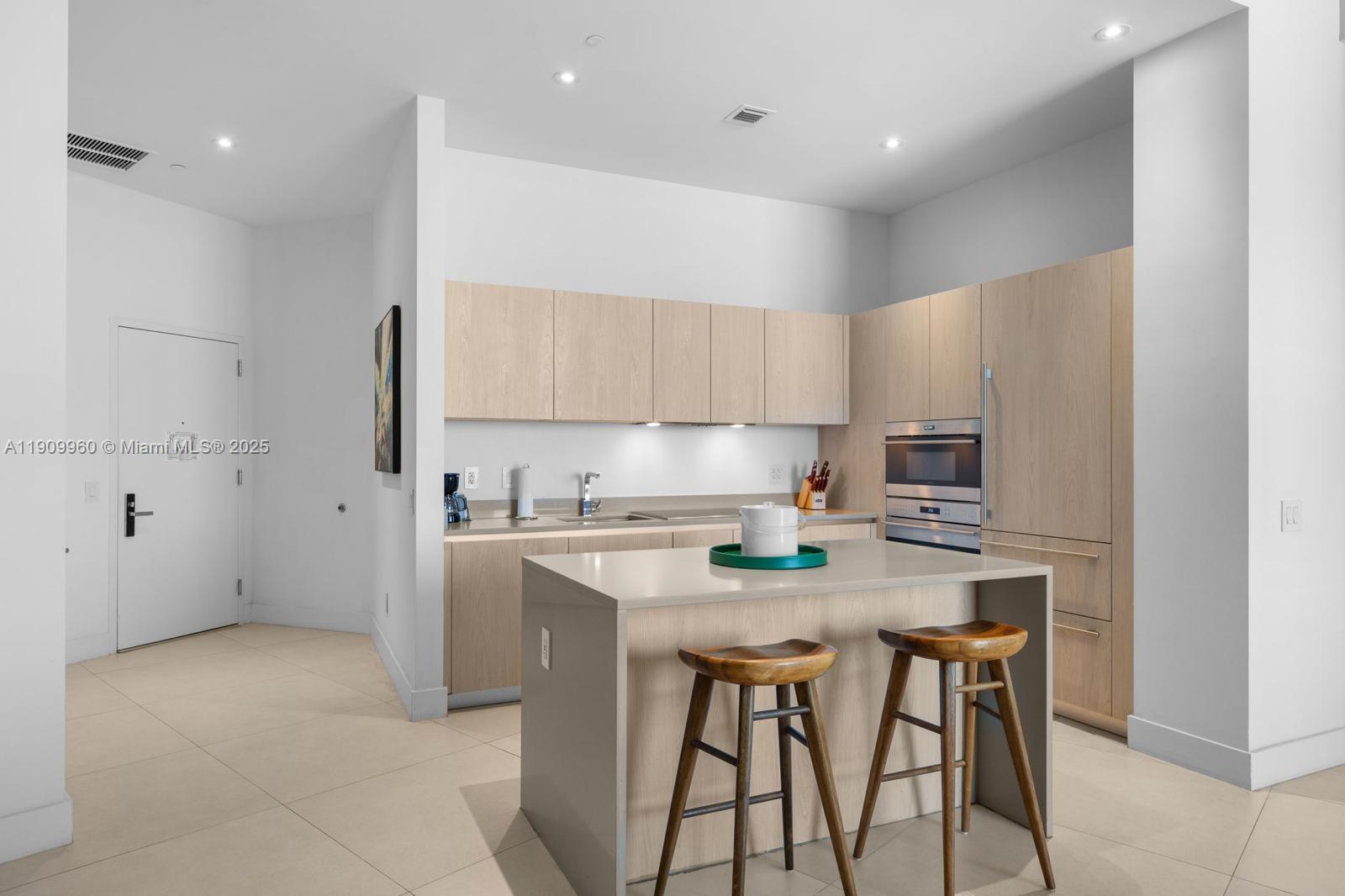 A modern kitchen features light wood cabinetry, a central island with bar stools, and tile flooring — 4111 S Ocean Dr # 502, Hollywood FL 33019, HOLLYWOOD, FL