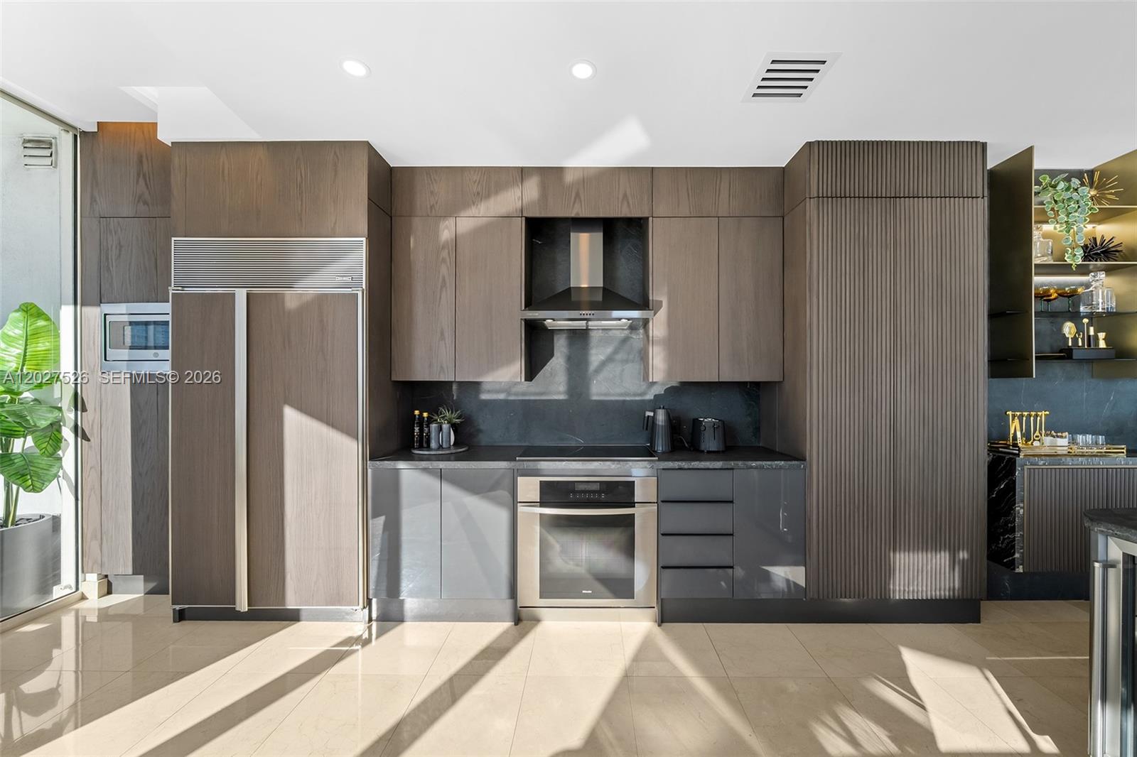 A modern kitchen features dark wood cabinetry, stainless steel appliances, and a black stone backsplash — 901 Brickell Key Blvd # 3304, Miami FL 33131, MIAMI, FL