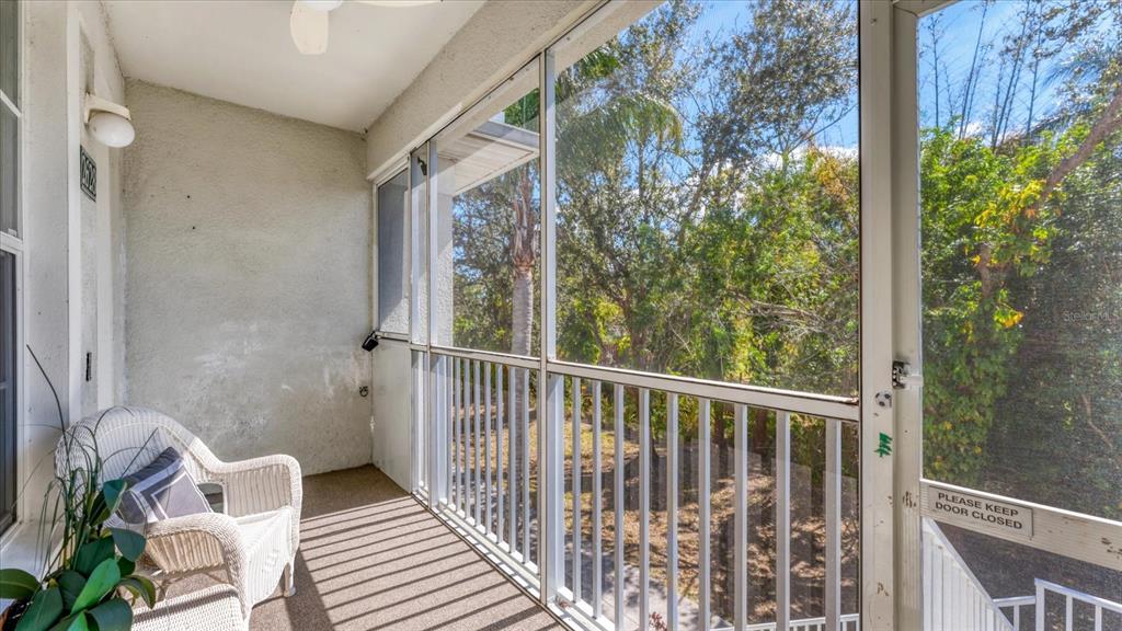 A screened-in balcony features a white wicker chair, carpeted flooring, and views of trees — 2628 RIVER PRESERVE COURT UNIT 2628, BRADENTON, FL