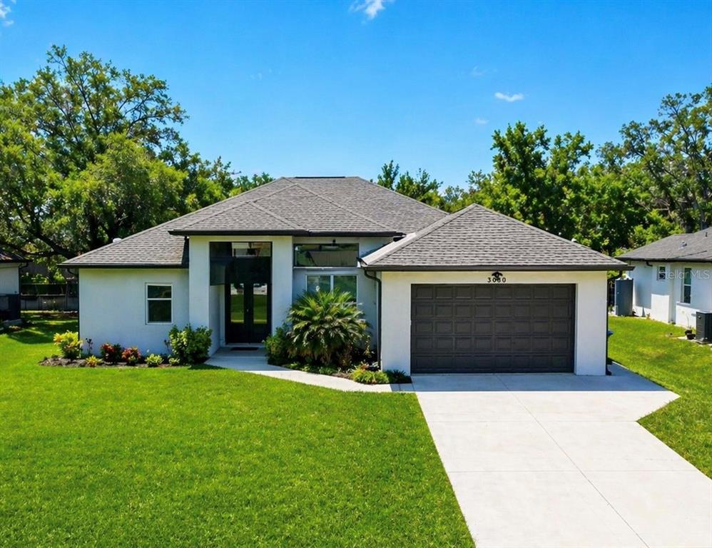 A single-story house with a white stucco exterior, a dark garage door, and a shingled roof — 3090 QUARTER STREET, NORTH PORT, FL