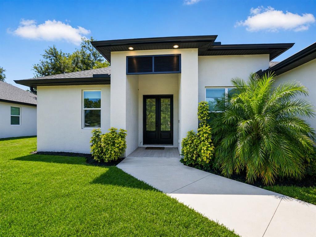 A modern single-story house exterior features a white stucco facade, black trim, and double doors — 3090 QUARTER STREET, NORTH PORT, FL