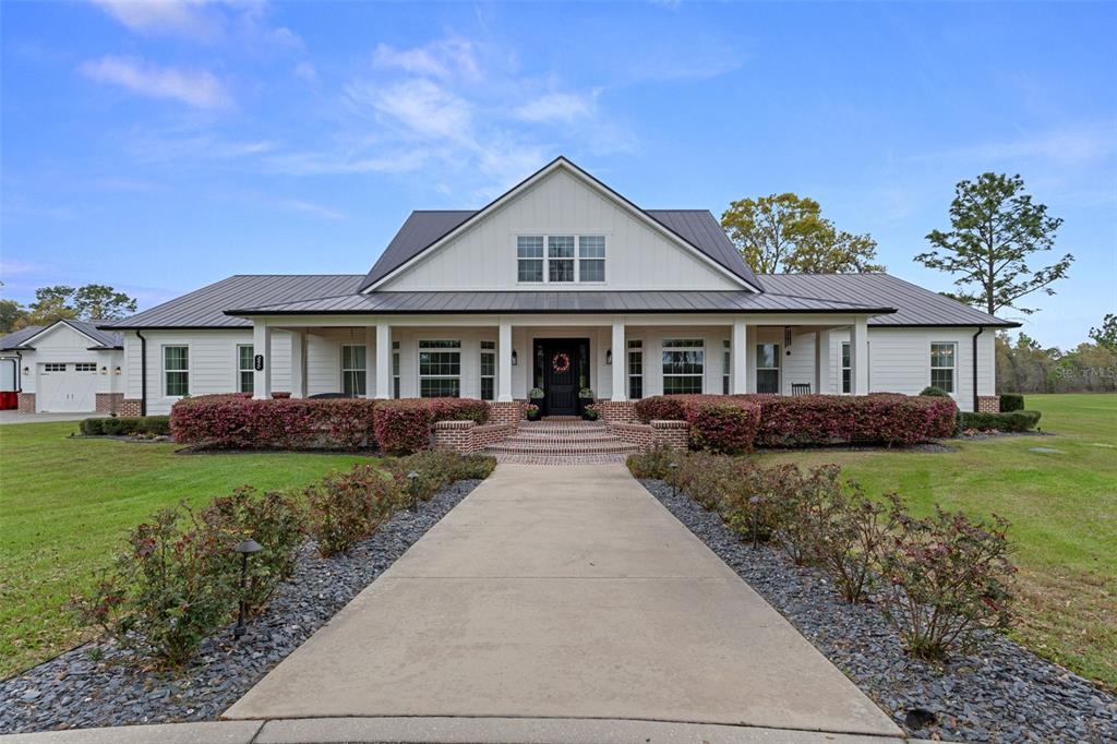 A white farmhouse with a metal roof and a brick-bordered walkway leading to the entrance — 2870 NW 87TH AVENUE, WILDWOOD, FL
