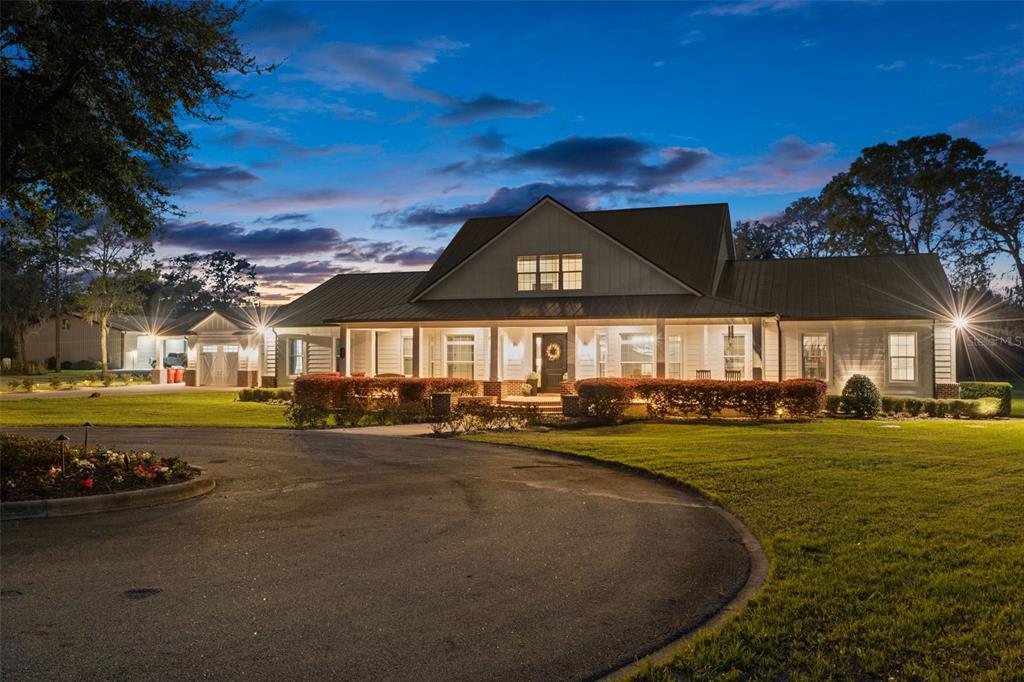 A wide, single-story house with a metal roof and front porch at twilight — 2870 NW 87TH AVENUE, WILDWOOD, FL