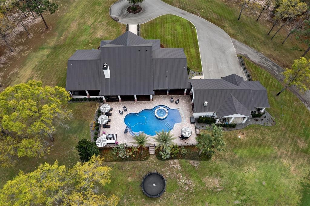 An aerial view shows a house with a dark metal roof, pool, and trampoline — 2870 NW 87TH AVENUE, WILDWOOD, FL