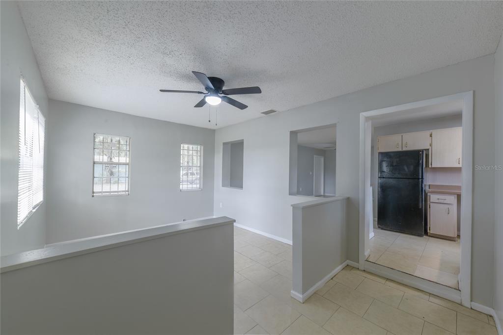 A living area with light-colored walls, tile flooring, and a ceiling fan leads to a kitchen — 14341 DELMAR STREET, DADE CITY, FL