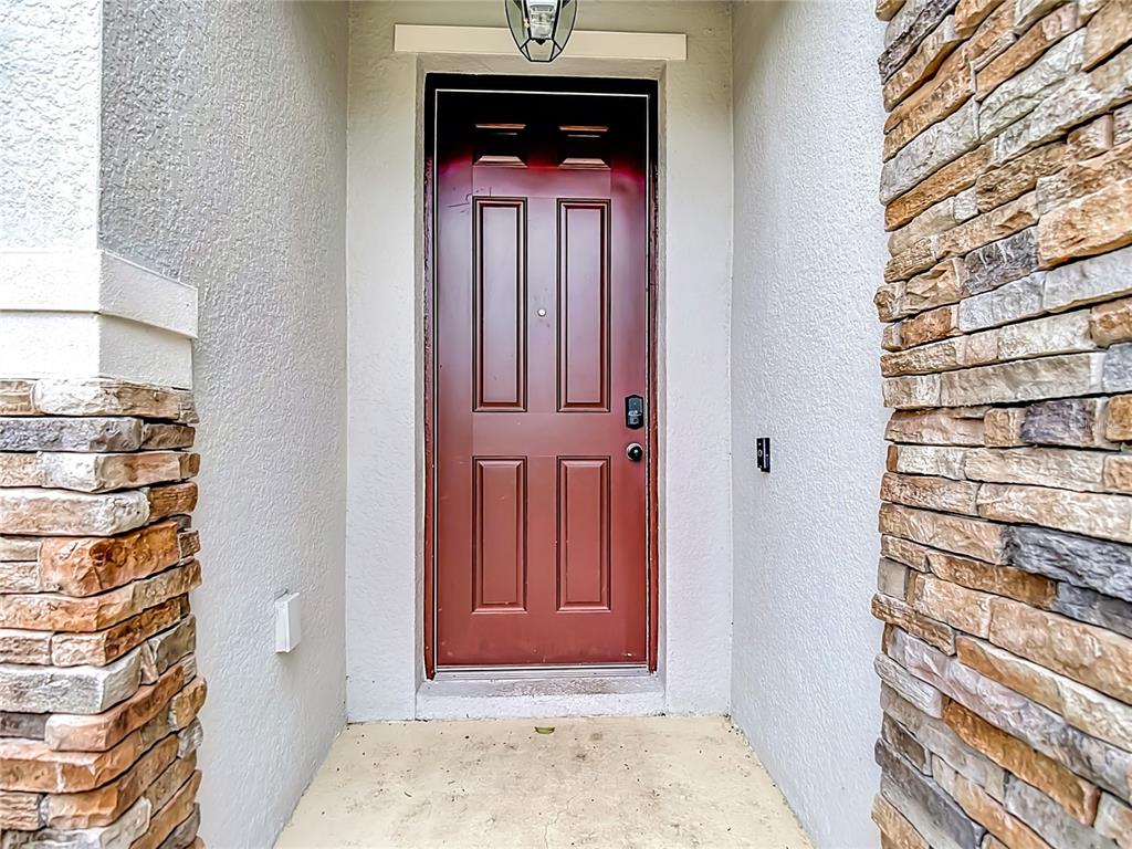 A red front door is framed by stone veneer pillars and light-colored stucco walls — 9127 FREEDOM HILL DRIVE, SEFFNER, FL