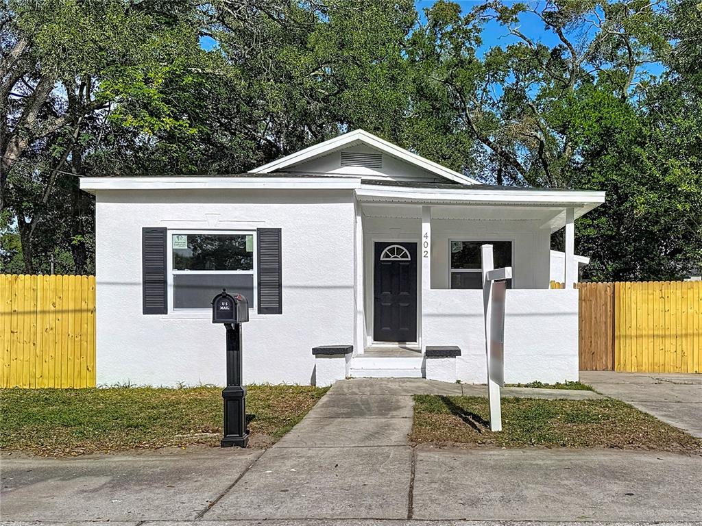 A white, single-story house with a black front door, shutters, and a yellow wooden fence — 402 E VIRGINIA AVENUE, TAMPA, FL