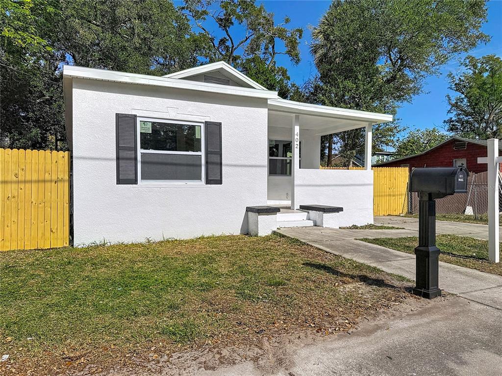 A small white house with a front porch, black shutters, and a yellow wooden fence — 402 E VIRGINIA AVENUE, TAMPA, FL