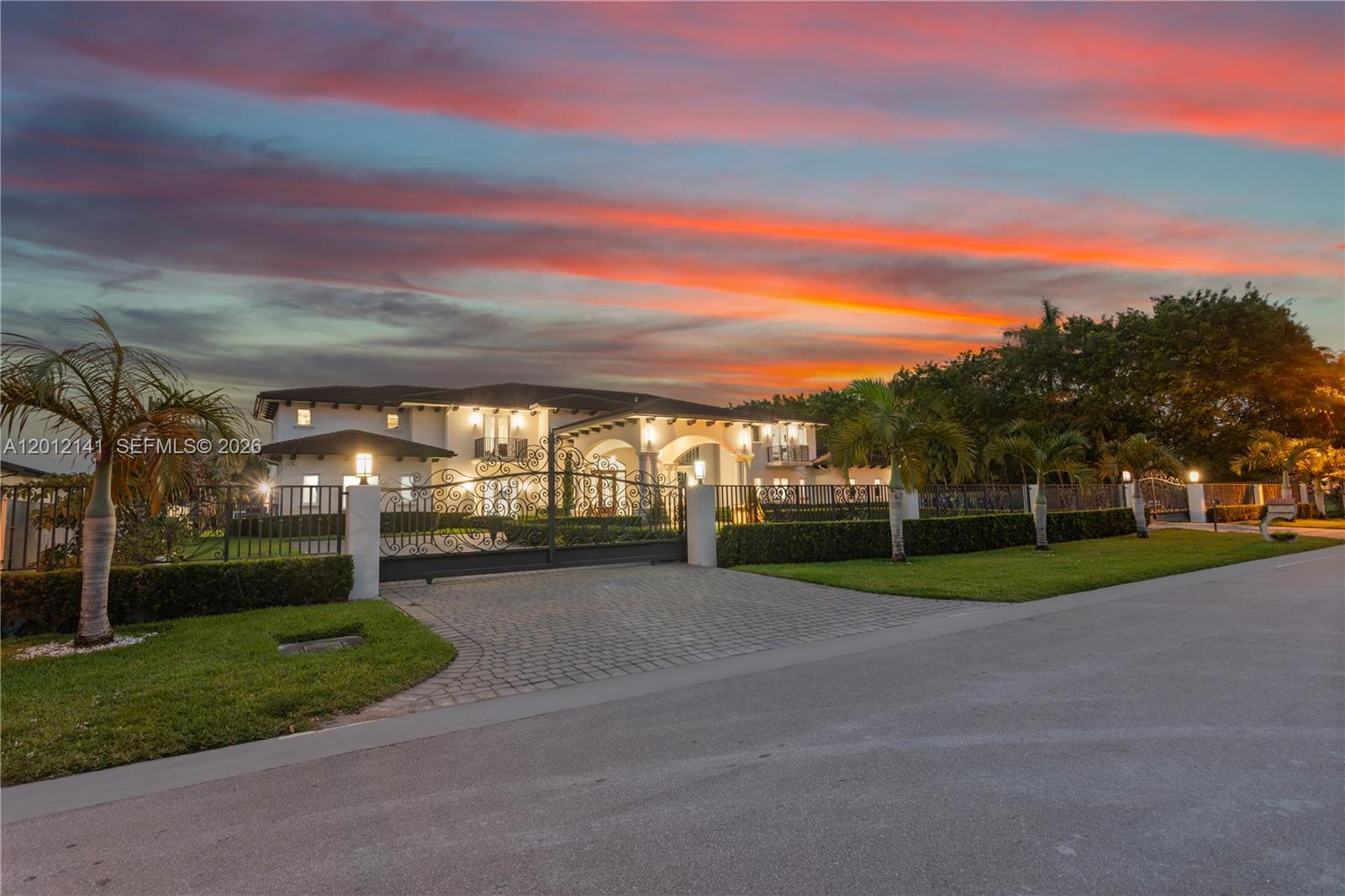 A large two-story house with a gated driveway is viewed at sunset — 12401 SW 45th St, Miami FL 33175, MIAMI, FL