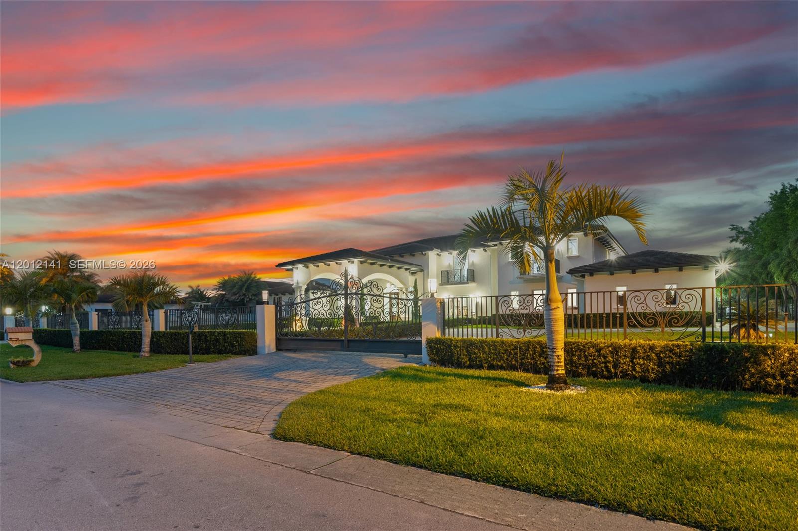 A gated two-story house with a paved driveway sits behind a fence at sunset — 12401 SW 45th St, Miami FL 33175, MIAMI, FL