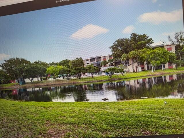 A multi-story apartment building sits behind a pond with a grassy foreground — 2308 S Cypress Bend Drive # 123, Pompano Beach FL 33069, POMPANO BEACH, FL