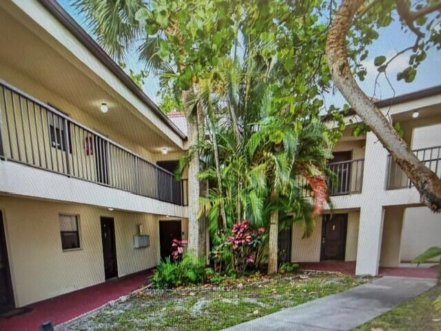 An exterior view of a two-story apartment complex with a central courtyard and palm trees — 2308 S Cypress Bend Drive # 123, Pompano Beach FL 33069, POMPANO BEACH, FL