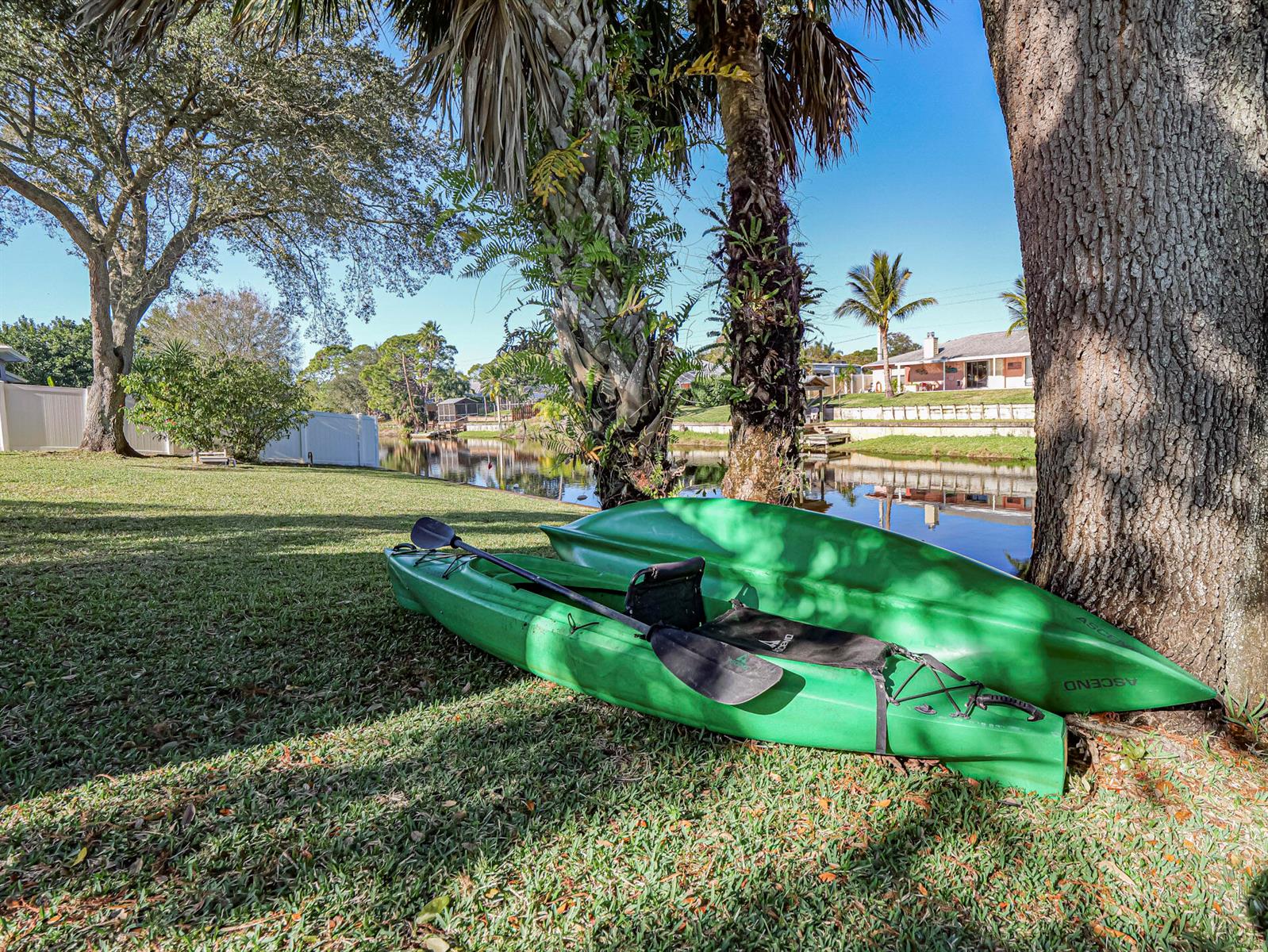 Two green kayaks rest on the grass near a canal and large trees — 255 Joy Haven Drive, Sebastian FL 32958, SEBASTIAN, FL