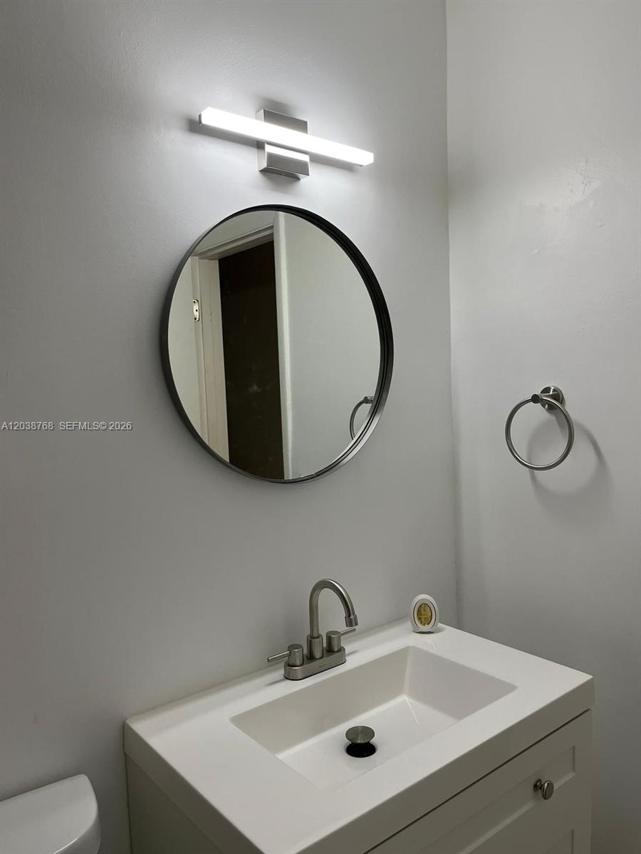 A bathroom features a white vanity, a round mirror, and a modern wall-mounted light fixture — 325 NE 2 # 5, Hallandale Beach FL 33009, HALLANDALE BEACH, FL