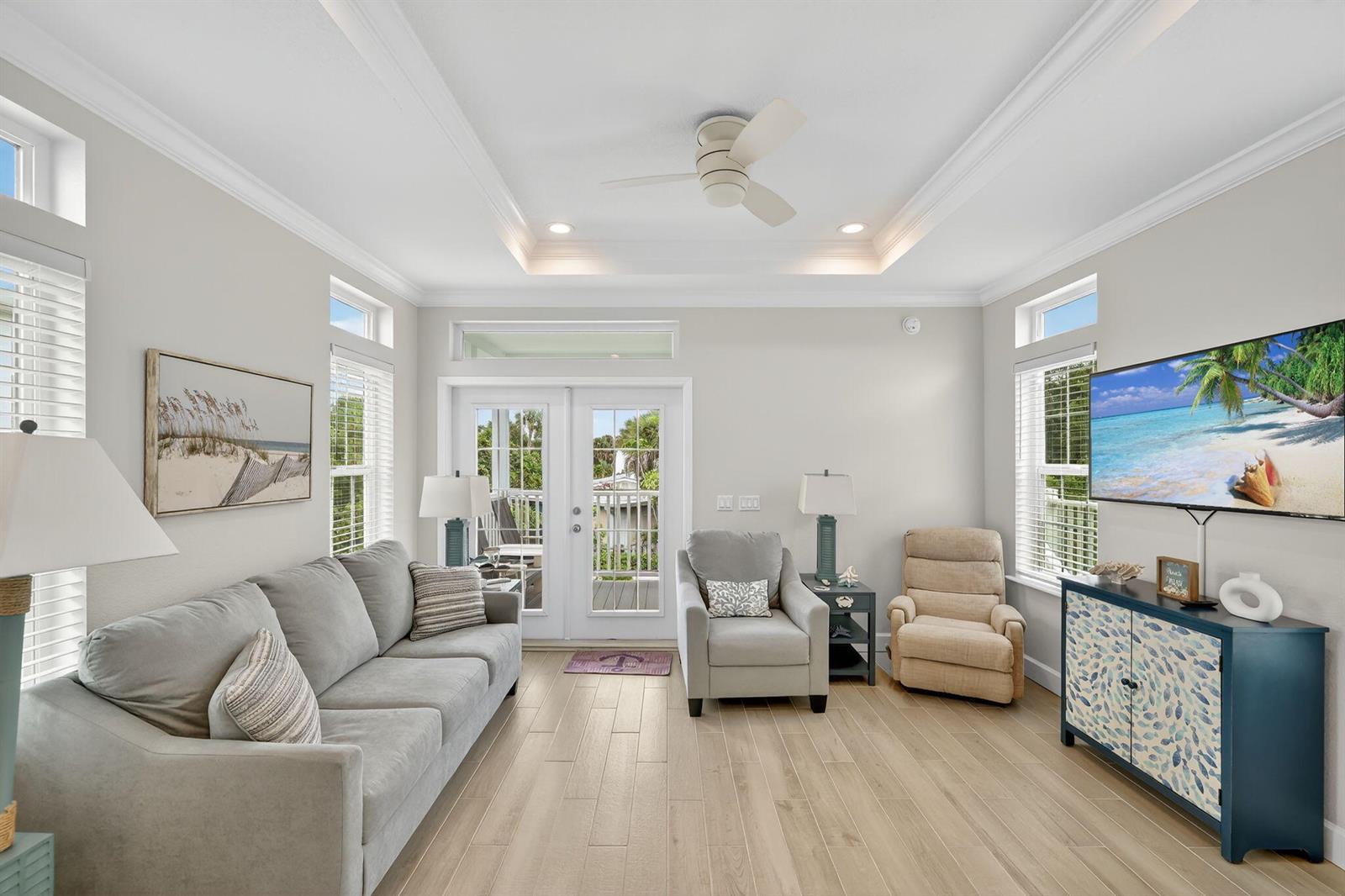 A living room features a gray sofa, two armchairs, a television, and light wood flooring — 300 NE Coastal Drive, Jensen Beach FL 34957, JENSEN BEACH, FL