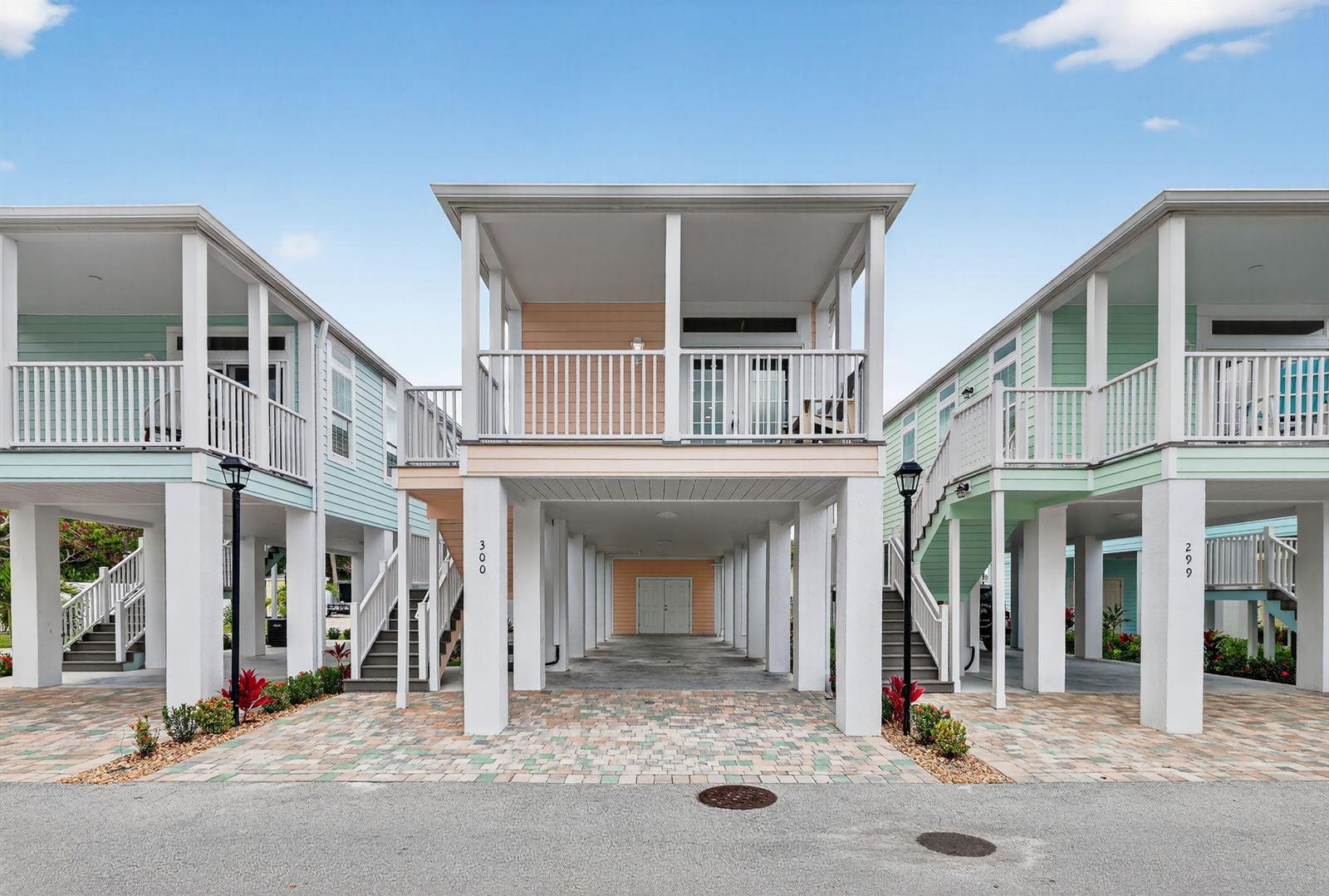 Three elevated coastal houses with pastel siding and ground-level parking stand side-by-side under a blue sky — 300 NE Coastal Drive, Jensen Beach FL 34957, JENSEN BEACH, FL