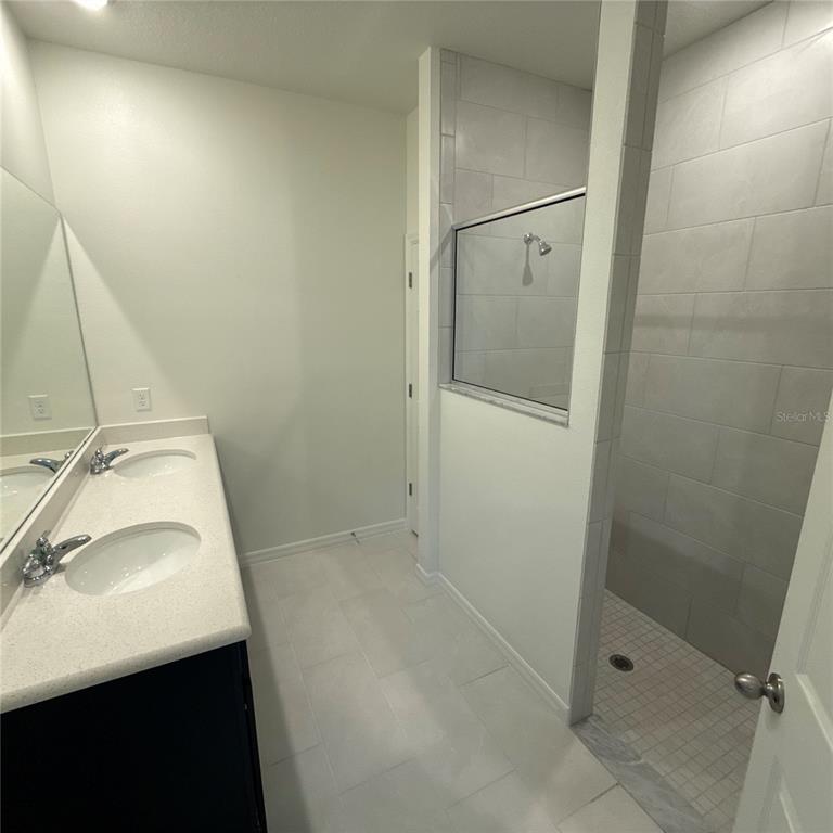 A bathroom features a double vanity with a white countertop and a tiled walk-in shower — 122 WELLSTONE DRIVE, PALM COAST, FL