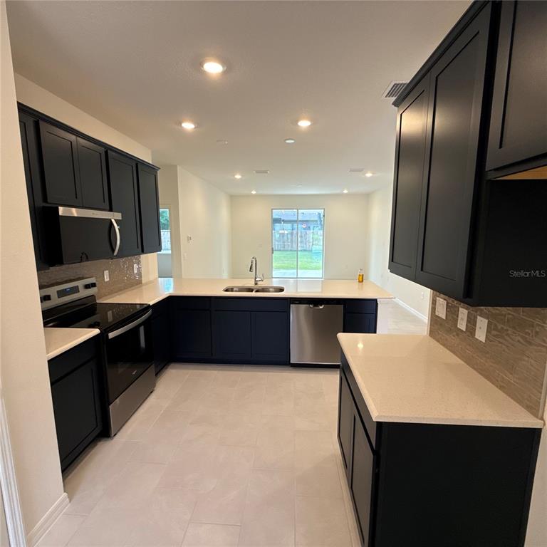 A kitchen features black cabinets, light countertops, stainless steel appliances, and light-colored tile flooring — 122 WELLSTONE DRIVE, PALM COAST, FL