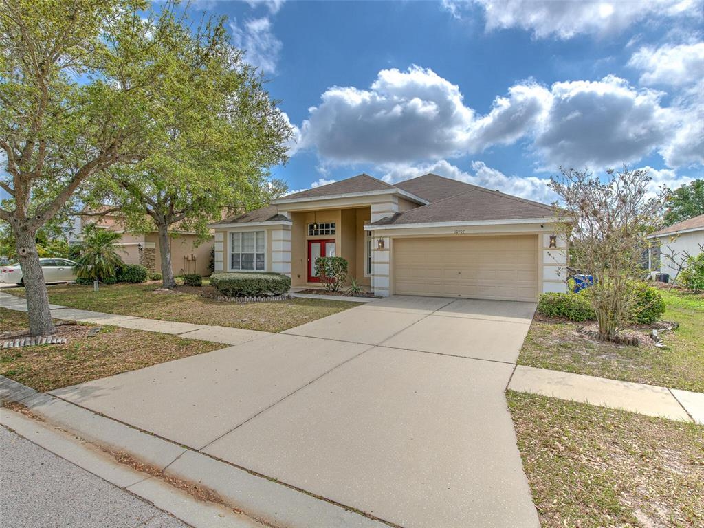 A single-story suburban house with a tan exterior, a red front door, and a driveway — 10907 AUSTRALIAN PINE DRIVE, RIVERVIEW, FL