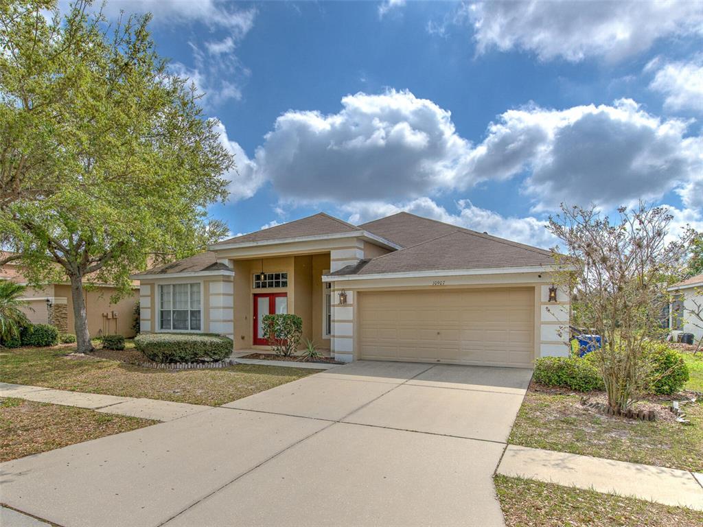 A single-story suburban house with a beige stucco exterior, a two-car garage, and a red door — 10907 AUSTRALIAN PINE DRIVE, RIVERVIEW, FL