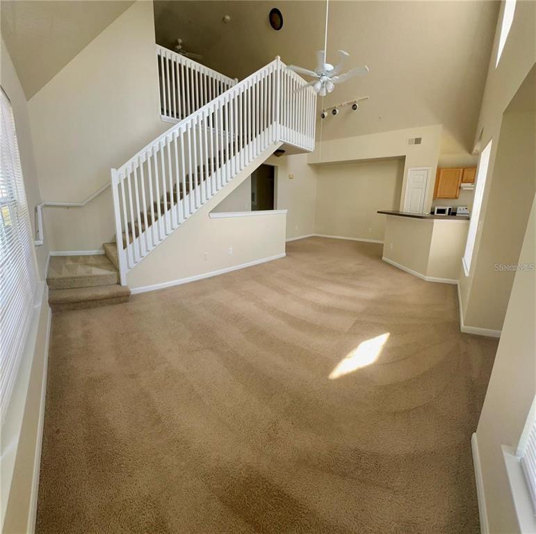 A living room with beige carpeting, a white staircase, and an open kitchen area — 9021 LEE VISTA BOULEVARD UNIT 1711, ORLANDO, FL