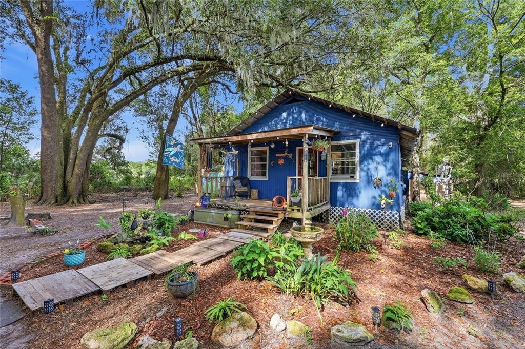A blue cottage with a wooden porch sits among large trees in a wooded yard — 10222 NW 173RD STREET, ALACHUA, FL