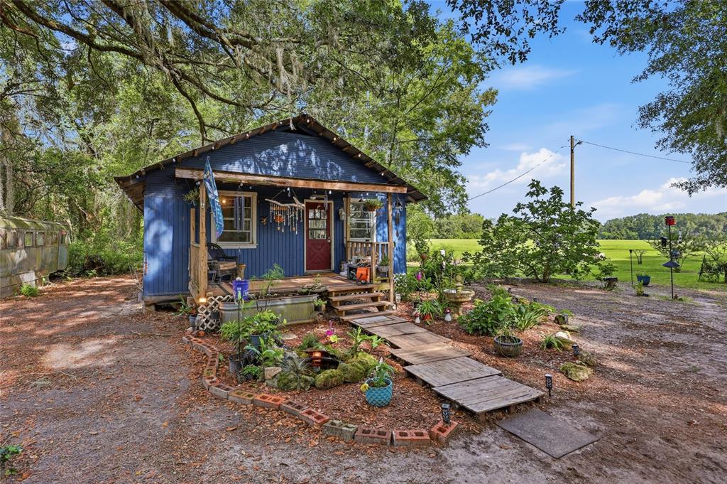 A small blue house with a front porch, wooden walkway, and a landscaped garden area — 10222 NW 173RD STREET, ALACHUA, FL