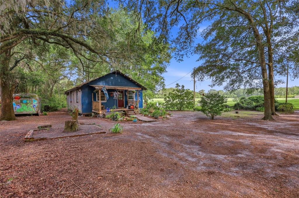 A blue house with a front porch sits on a dirt lot under large trees — 10222 NW 173RD STREET, ALACHUA, FL