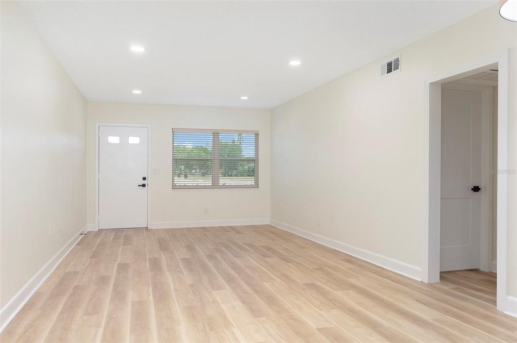 A bright, empty room features light wood-look flooring, white walls, recessed lighting, and a window — 3740 58TH STREET N UNIT 106, ST PETERSBURG, FL