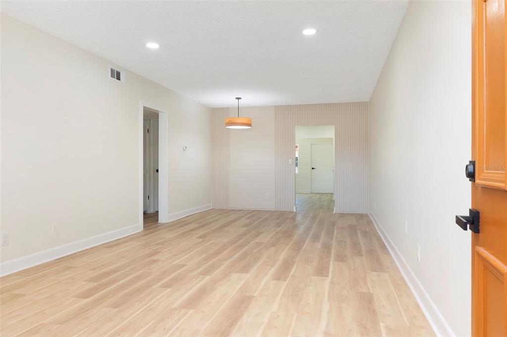 An empty room with light wood-look flooring, a modern pendant light, and vertical wall paneling — 3740 58TH STREET N UNIT 106, ST PETERSBURG, FL
