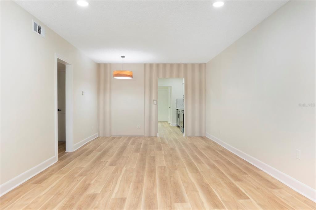 An empty dining room features light wood-look flooring, a modern pendant light, and slatted wall paneling — 3740 58TH STREET N UNIT 106, ST PETERSBURG, FL