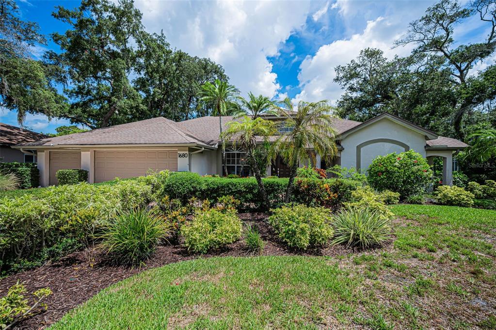 A single-story house with a tan garage, palm trees, and landscaped front yard — 1680 SPARKLING COURT, DUNEDIN, FL