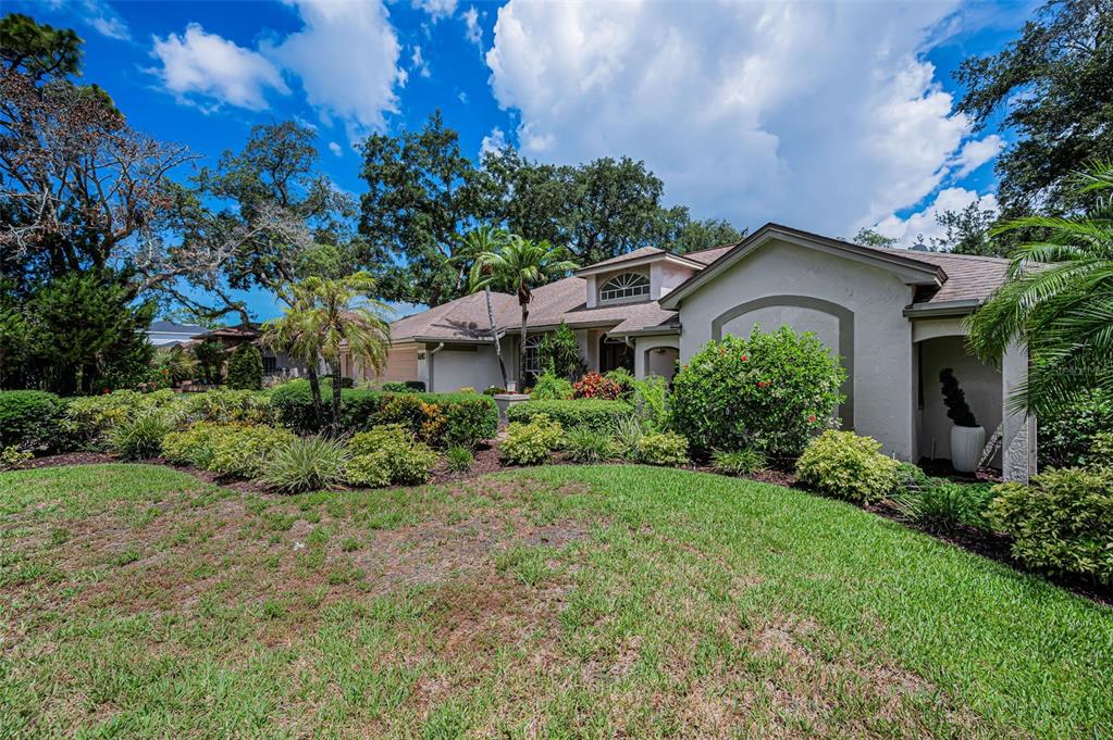 A single-story house with a beige stucco exterior, a tiled roof, and lush landscaping — 1680 SPARKLING COURT, DUNEDIN, FL