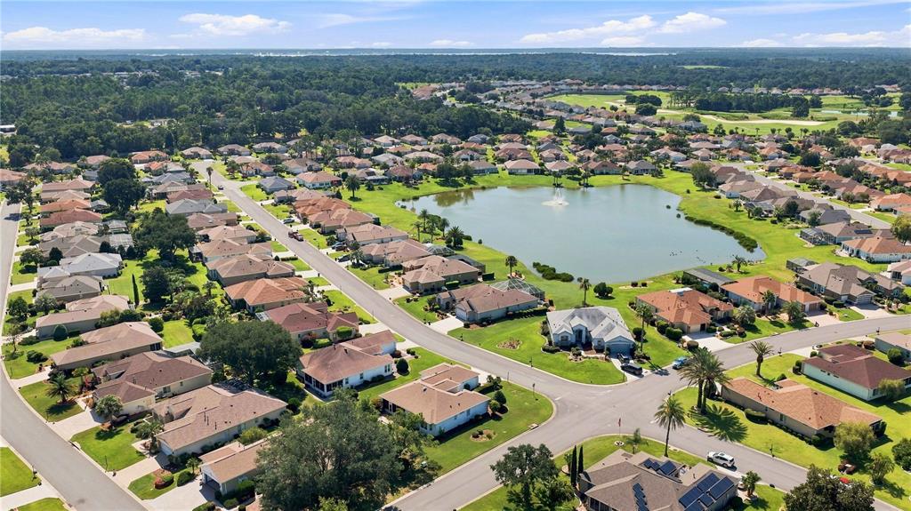 An aerial view of a suburban neighborhood featuring houses surrounding a central pond with fountain — 9317 124TH PLACE, SUMMERFIELD, FL