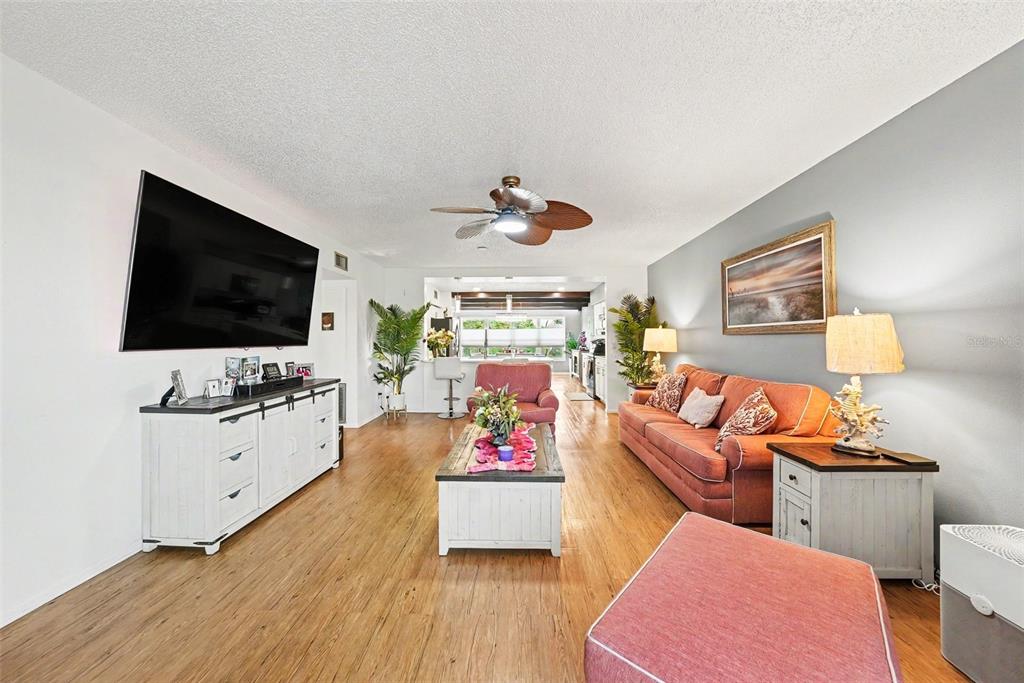 A living room features wood-look flooring, a large television, an orange sofa, and a ceiling fan — 2284 PHILIPPINE DRIVE UNIT 69, CLEARWATER, FL