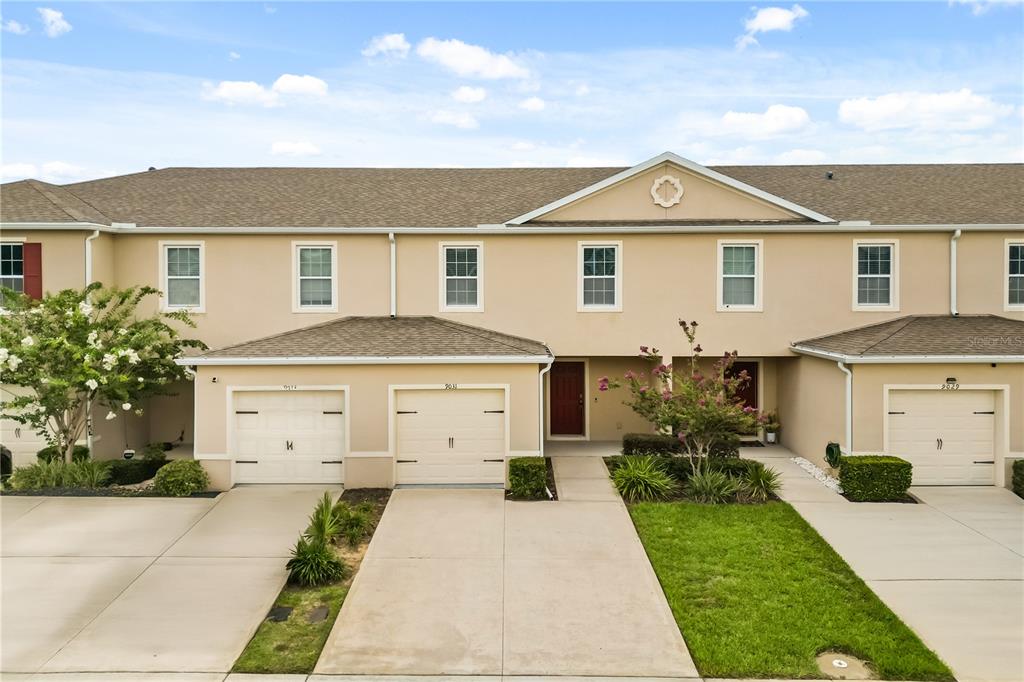 An exterior view of a multi-unit townhouse complex with beige stucco walls and garages — 9031 WILDFLOWER LANE, KISSIMMEE, FL