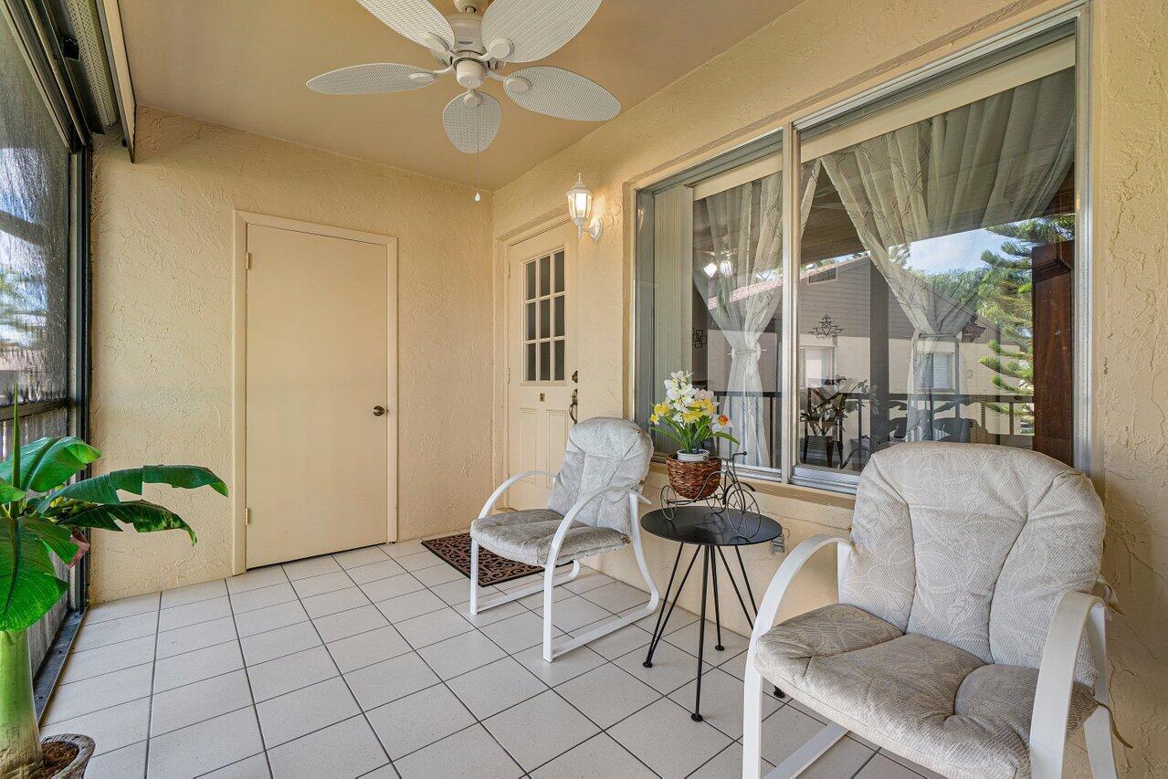 A screened-in patio features tiled flooring, two cushioned chairs, a small table, and a ceiling fan — 407 Pine Glen Lane # 1, FL 33463, FL