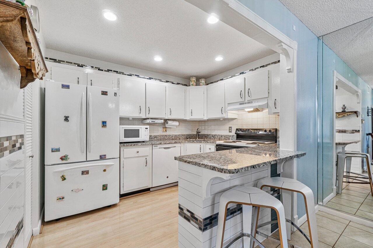 A kitchen with white cabinets, granite countertops, a breakfast bar, and stainless steel appliances — 407 Pine Glen Lane # 1, FL 33463, FL