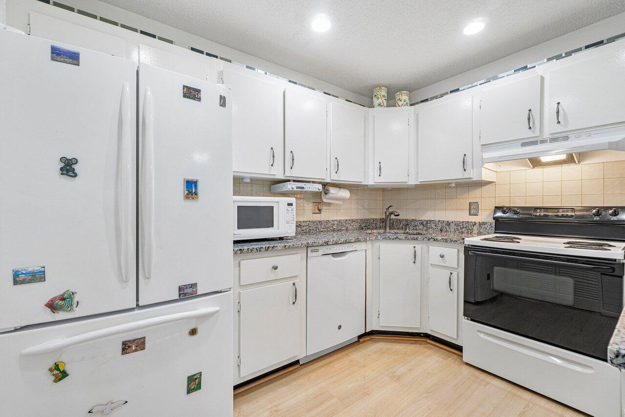 A kitchen features white cabinets, granite countertops, a white refrigerator, and a black electric stove — 407 Pine Glen Lane # 1, FL 33463, FL