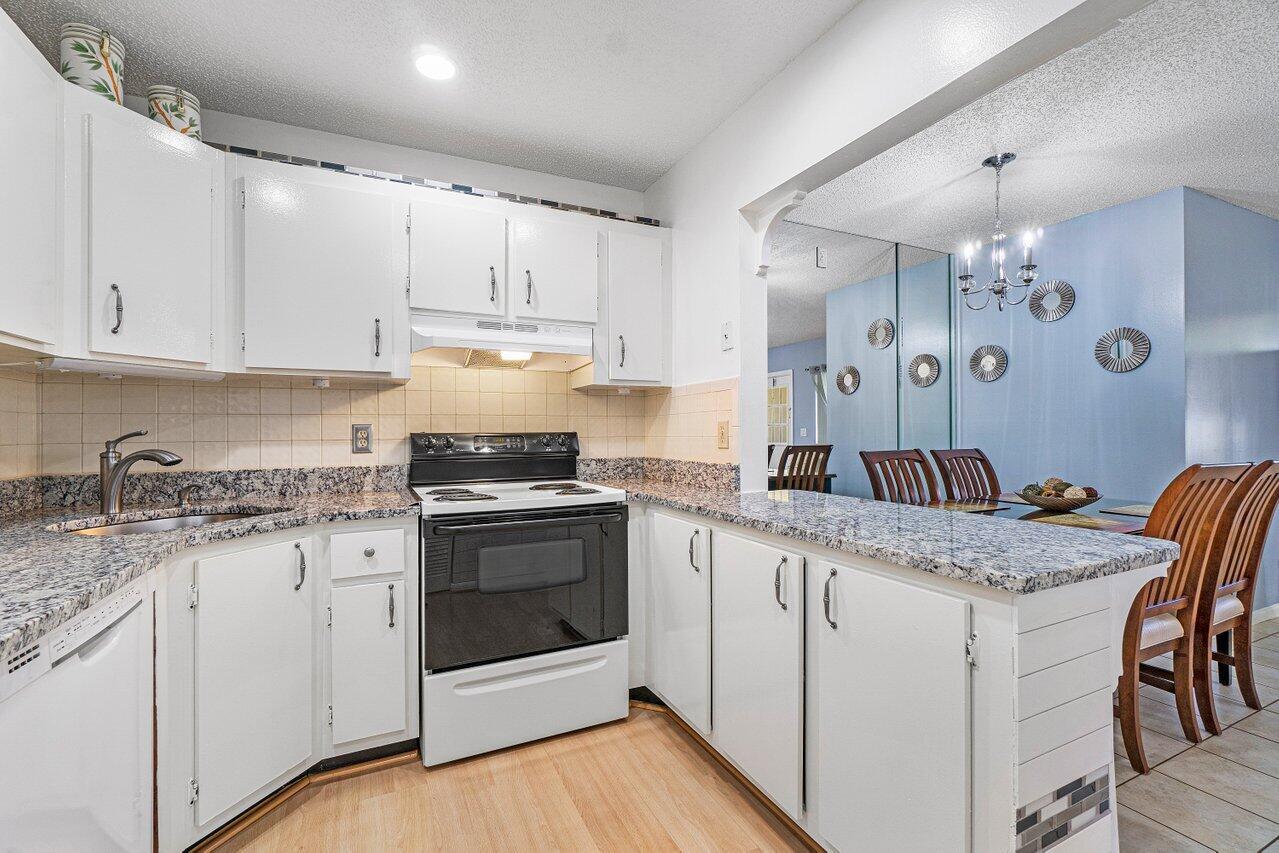 A kitchen with white cabinets, granite countertops, and a pass-through to the dining area — 407 Pine Glen Lane # 1, FL 33463, FL
