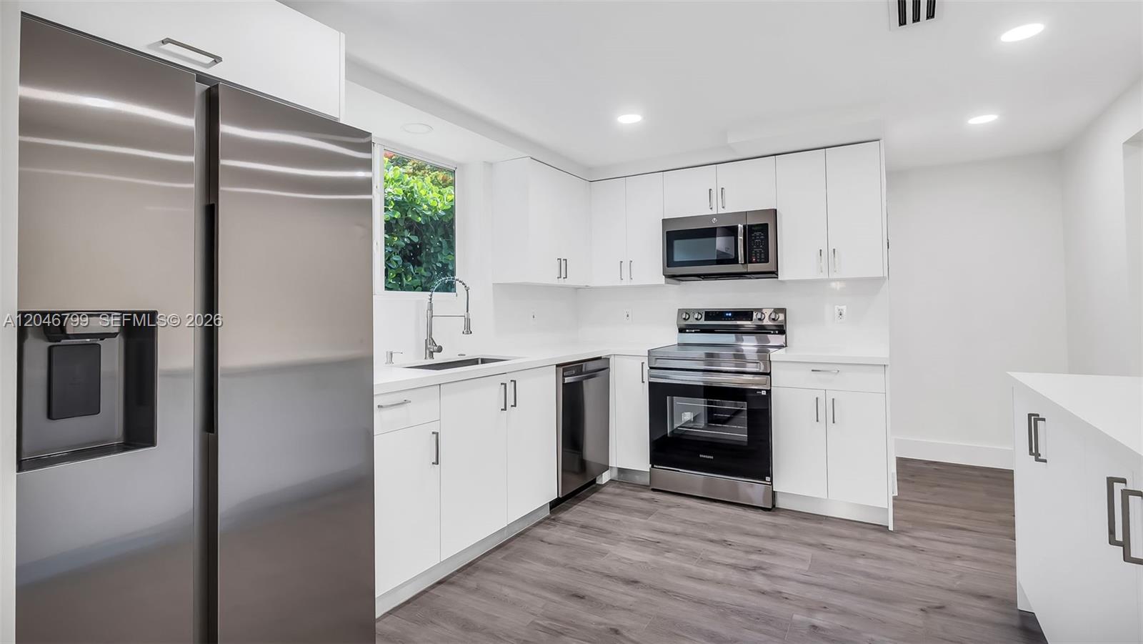 A modern kitchen features white cabinets, stainless steel appliances, and wood-look flooring — 1500 NE 13th Pl, Miami FL 33139, MIAMI, FL